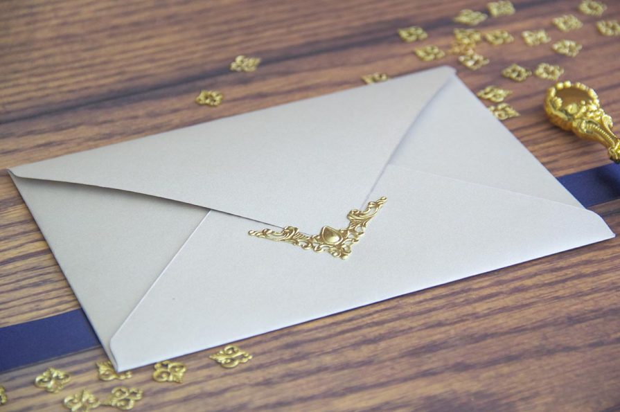 A imagem mostra a aproximação do envelope do convite de casamento vendo-se o pormenor da peça metálica.